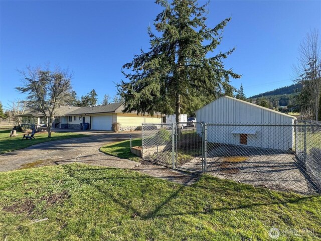 view of side of home featuring driveway, a gate, fence, and a lawn