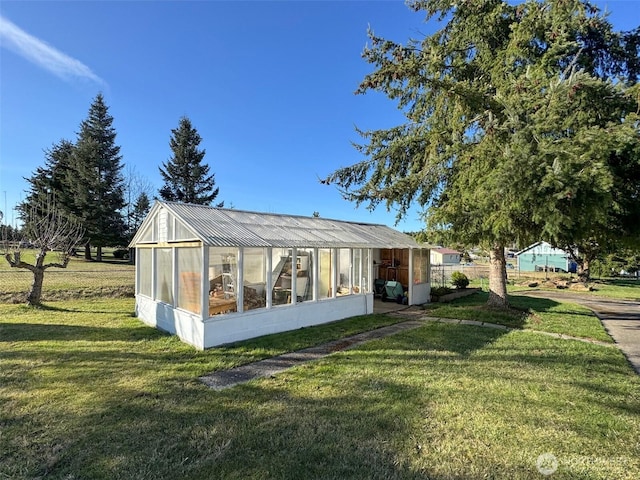 exterior space with a greenhouse, metal roof, a lawn, and an outbuilding