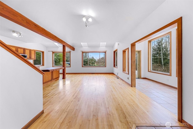 unfurnished living room featuring baseboards, beam ceiling, and light wood-style flooring