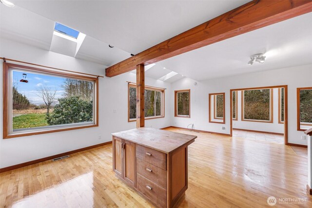 kitchen featuring visible vents, a center island, baseboards, lofted ceiling with skylight, and light wood-style flooring