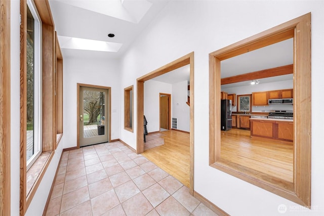 foyer entrance with light tile patterned floors, a skylight, a high ceiling, and baseboards