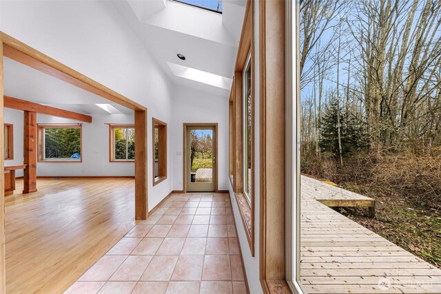 entrance foyer featuring a skylight, light tile patterned flooring, a healthy amount of sunlight, and high vaulted ceiling