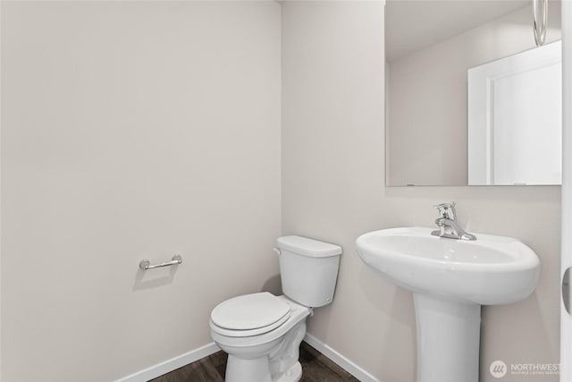 half bathroom with wood finished floors, toilet, and baseboards