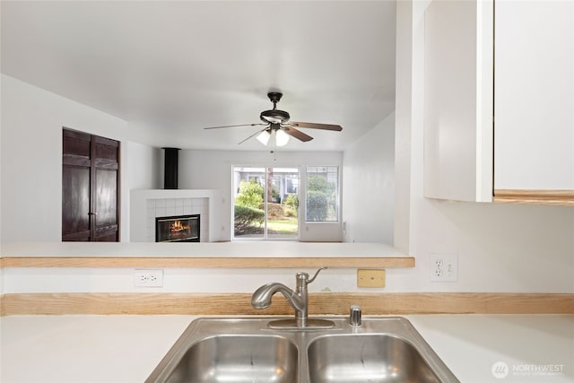 kitchen with a tiled fireplace, a ceiling fan, light countertops, and a sink