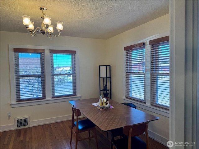 dining space featuring dark wood finished floors, a notable chandelier, visible vents, a textured ceiling, and baseboards