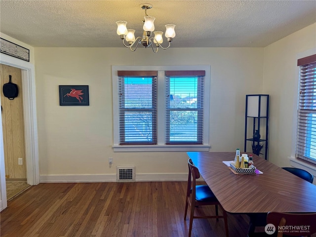 dining room featuring a chandelier, visible vents, a textured ceiling, and wood finished floors