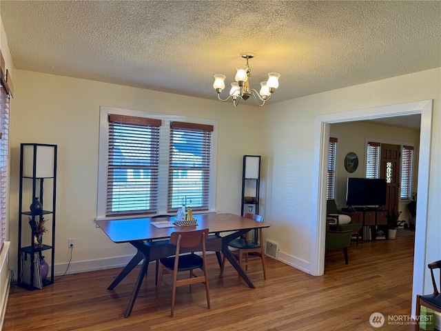 dining space with a notable chandelier, visible vents, a textured ceiling, wood finished floors, and baseboards