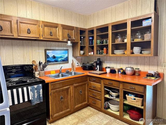 kitchen featuring a textured ceiling, black range with electric stovetop, a sink, light countertops, and brown cabinets