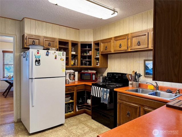 kitchen with light floors, brown cabinetry, freestanding refrigerator, a sink, and black / electric stove