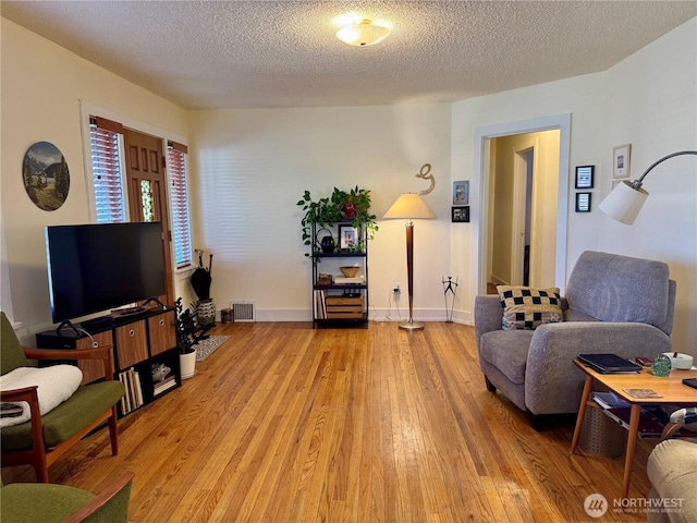 living area featuring a textured ceiling, baseboards, visible vents, and light wood-style floors