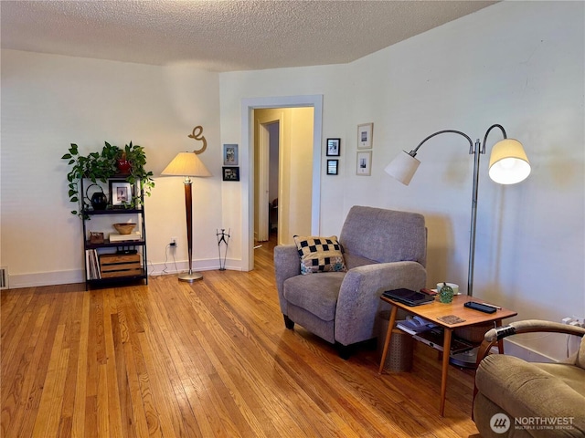 living area with a textured ceiling, light wood finished floors, visible vents, and baseboards