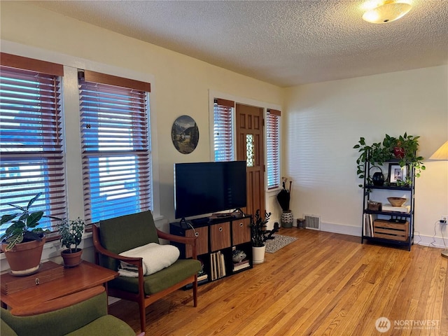 living area with light wood-style floors, visible vents, a textured ceiling, and baseboards