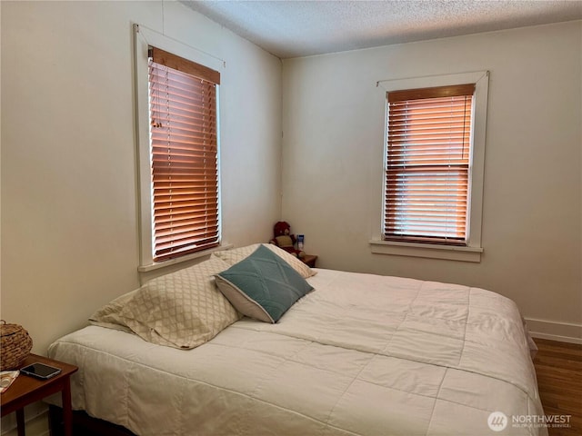 bedroom with a textured ceiling, wood finished floors, and baseboards