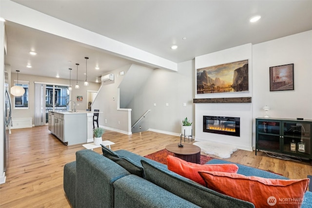 living room featuring light wood-type flooring, recessed lighting, an AC wall unit, and a glass covered fireplace