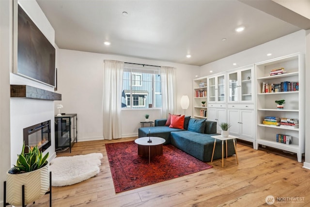 living room featuring light wood-type flooring, recessed lighting, baseboards, and a glass covered fireplace