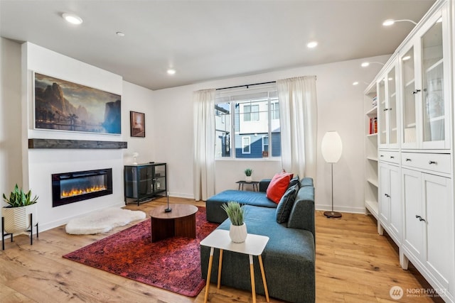 living area featuring light wood-type flooring, recessed lighting, baseboards, and a glass covered fireplace