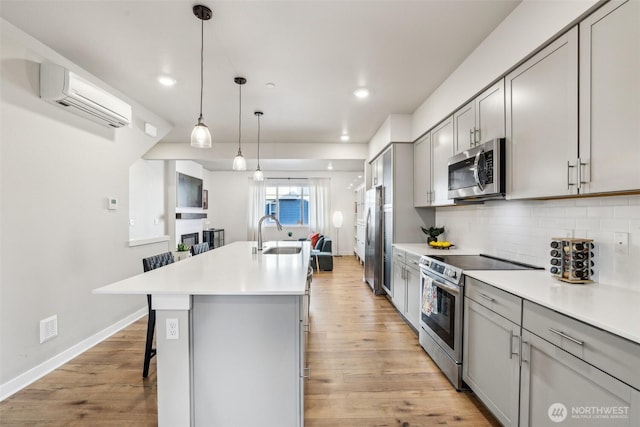 kitchen with appliances with stainless steel finishes, a wall mounted air conditioner, a sink, and gray cabinetry