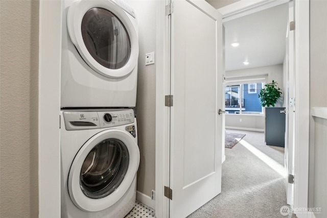 clothes washing area with laundry area, carpet floors, stacked washing maching and dryer, and baseboards