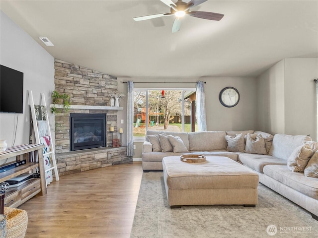 living area with visible vents, ceiling fan, wood finished floors, vaulted ceiling, and a fireplace