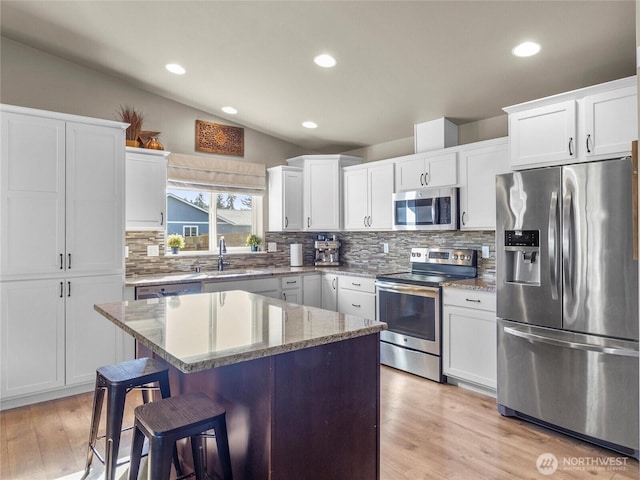 kitchen featuring a breakfast bar, a sink, vaulted ceiling, appliances with stainless steel finishes, and light wood-type flooring