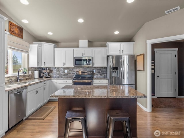 kitchen featuring visible vents, appliances with stainless steel finishes, a kitchen bar, white cabinetry, and a sink