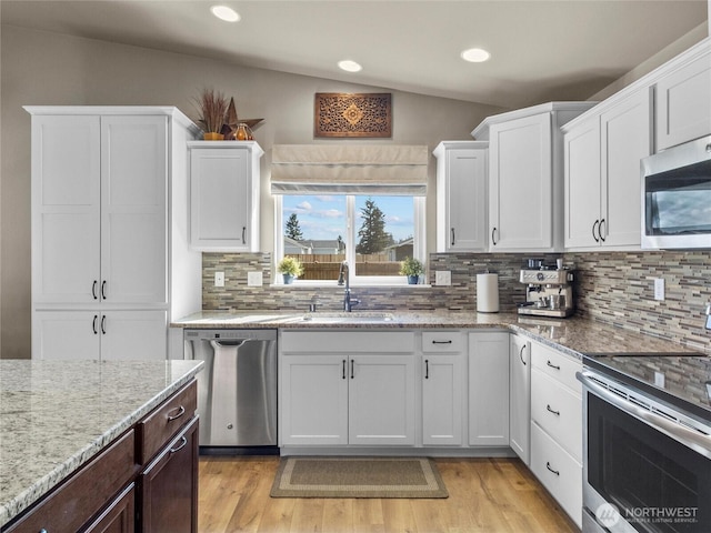 kitchen featuring stainless steel appliances, a sink, light wood-style floors, white cabinets, and light stone countertops