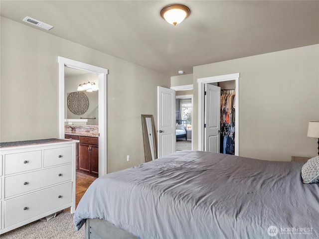 bedroom featuring a closet, visible vents, a spacious closet, light carpet, and ensuite bath