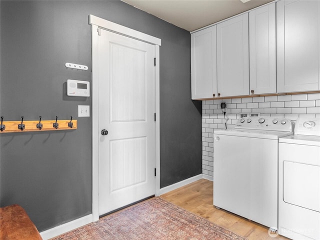 clothes washing area featuring light wood finished floors, separate washer and dryer, cabinet space, and baseboards