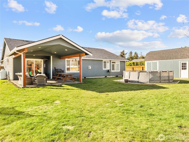 back of house featuring a covered pool, fence, a shingled roof, and a yard