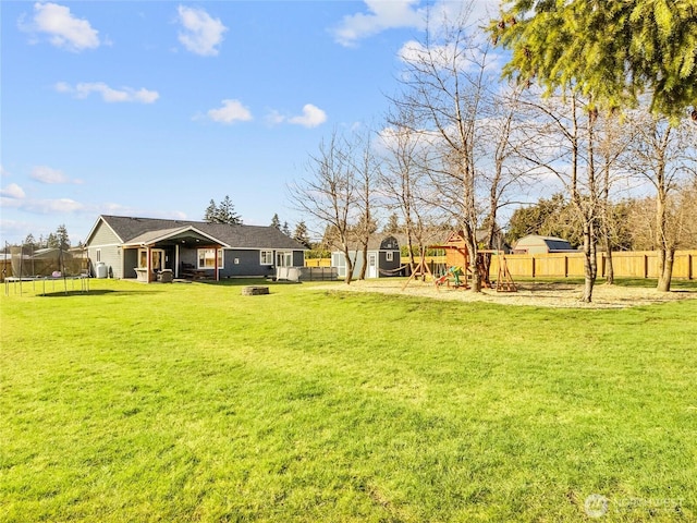 view of yard with a fenced backyard, a trampoline, a fire pit, and a playground