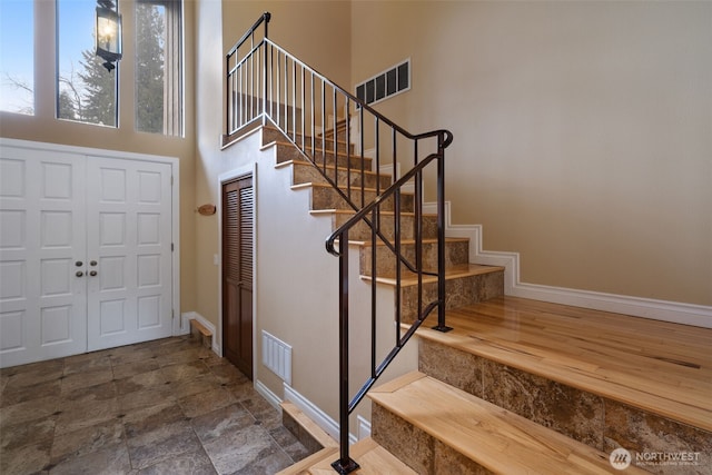 foyer entrance with a towering ceiling, baseboards, stairs, and visible vents