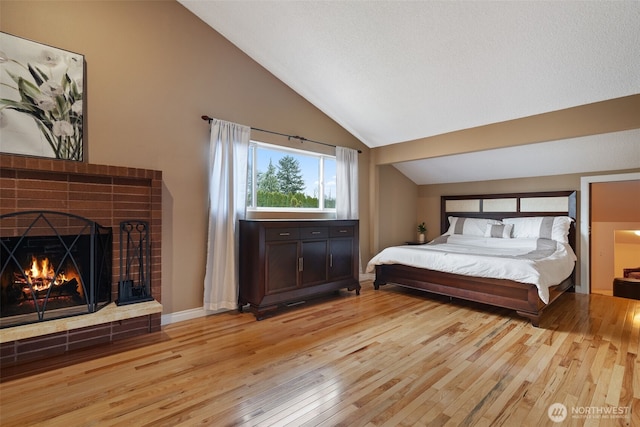 bedroom featuring vaulted ceiling, a brick fireplace, baseboards, and light wood-style floors