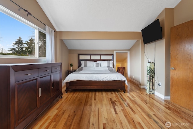 bedroom with lofted ceiling, light wood finished floors, and baseboards