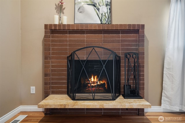 room details featuring a brick fireplace, visible vents, baseboards, and wood finished floors