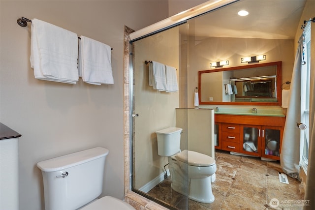 bathroom with toilet, a stall shower, stone finish flooring, and vanity