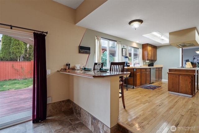 kitchen with brown cabinetry, dishwasher, a breakfast bar area, a peninsula, and a sink