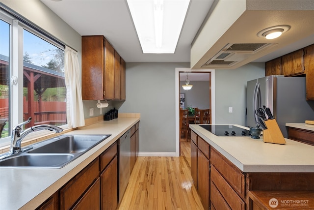 kitchen featuring light wood-style flooring, brown cabinets, stainless steel appliances, light countertops, and a sink