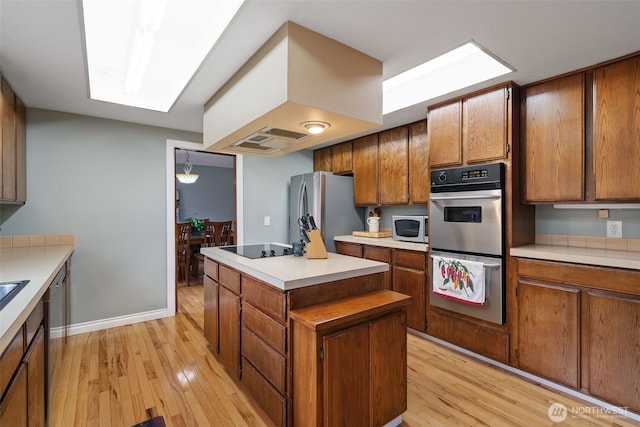 kitchen featuring appliances with stainless steel finishes, light countertops, brown cabinetry, and light wood finished floors