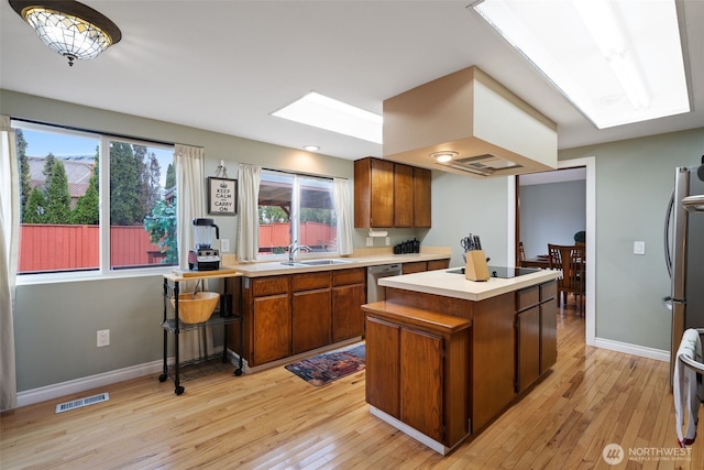 kitchen featuring a skylight, brown cabinets, light countertops, visible vents, and appliances with stainless steel finishes