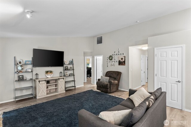 living area with visible vents, lofted ceiling, baseboards, and light wood finished floors