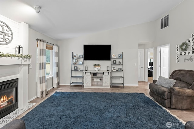 living room with baseboards, visible vents, a fireplace with flush hearth, vaulted ceiling, and light wood-type flooring