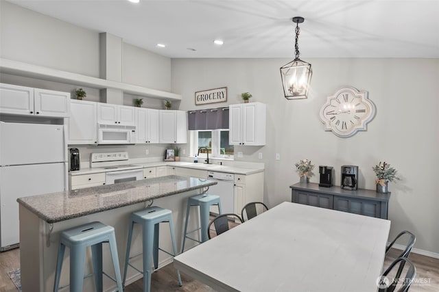 kitchen featuring a sink, a center island, white cabinetry, white appliances, and a breakfast bar area