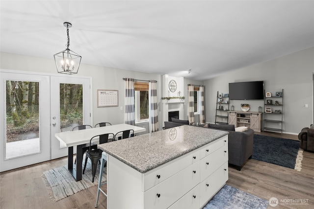 kitchen with light wood-type flooring, a kitchen island, a fireplace, and french doors