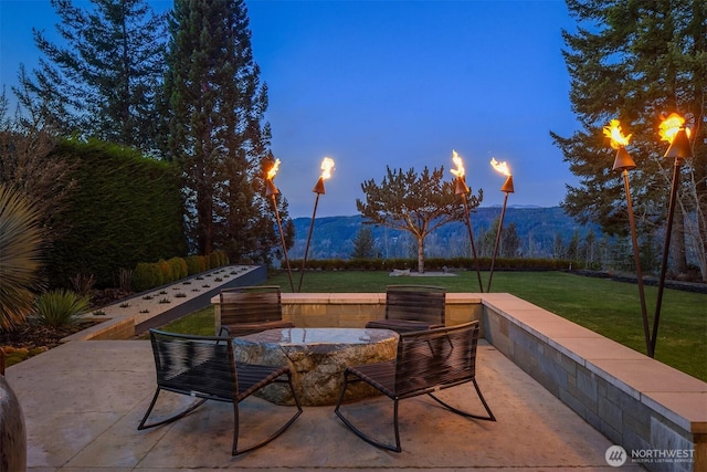 patio terrace at dusk featuring a lawn and a mountain view