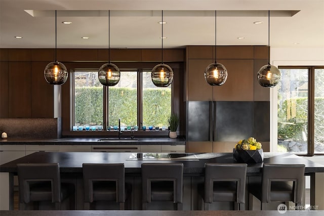 kitchen featuring modern cabinets, pendant lighting, a sink, a kitchen breakfast bar, and dark countertops