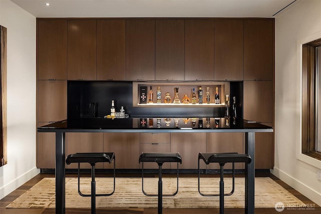 bar featuring dark wood-style floors, backsplash, a bar, and baseboards