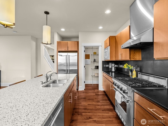 kitchen with dark stone counters, wall chimney exhaust hood, dark wood-type flooring, built in appliances, and a sink