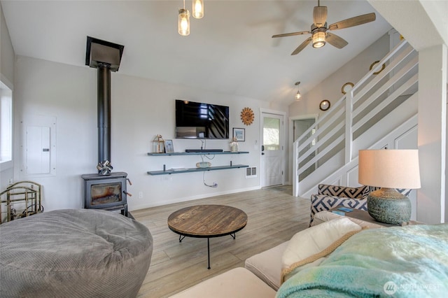 living room featuring electric panel, visible vents, stairway, wood finished floors, and a wood stove