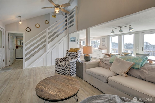 living room featuring ceiling fan, high vaulted ceiling, light wood-style floors, stairs, and track lighting