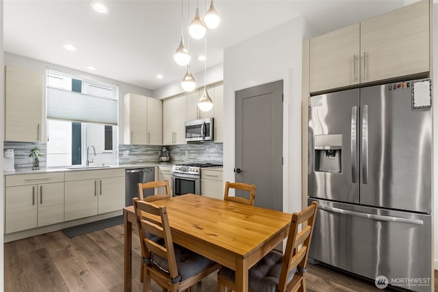 kitchen featuring stainless steel appliances, a sink, light countertops, decorative backsplash, and dark wood-style floors